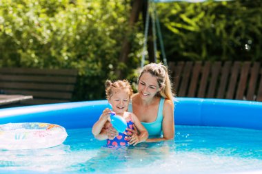Anne ve kızı sıcak bir yaz gününde arka bahçedeki havuzda oynuyorlar.