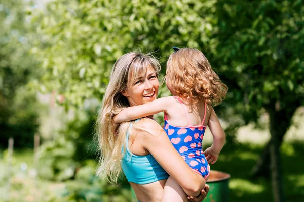 Uma jovem mãe segura sua filhinha em seus braços em um dia de verão no jardim ou parque — Fotografia de Stock