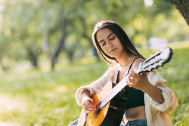 Kendisiyle uyum içinde olan bir kız parkta gitar çalar. Hobiler, müzik, müzisyen