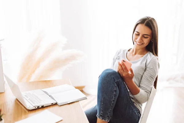 Retrato de uma linda menina sorridente sentada a uma mesa com um telefone na mão — Fotografia de Stock