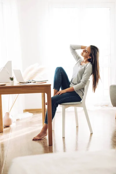 Uma linda garota está sentada inclinada para trás em uma cadeira e se alongando depois do trabalho em um laptop — Fotografia de Stock