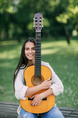 Elinde gitar tutan ve gülümseyen genç bir gitaristin portresi. Kız-müzisyen, müzik, hobi