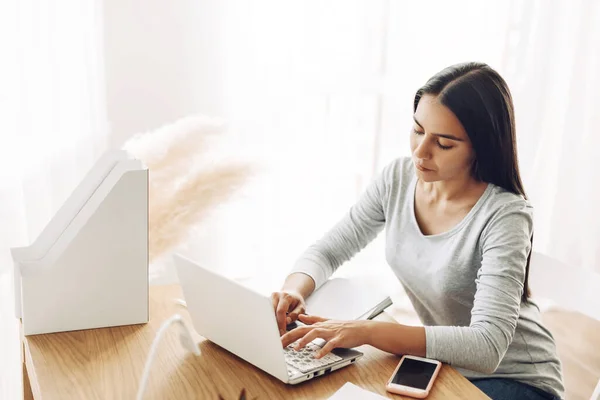 Um jovem estudante sentado em uma mesa usa um laptop enquanto estuda — Fotografia de Stock