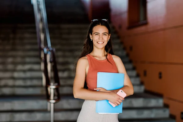 Una joven estudiante en ropa casual con un ensayo en una carpeta y un teléfono en sus manos — Foto de Stock