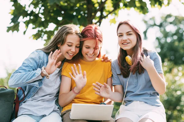 Trzy nastolatki komunikują się ze swoimi przyjaciółmi i kolegami przez łącze wideo za pomocą laptopa w parku. Przyjaciele, przyjaźń, czas razem — Zdjęcie stockowe