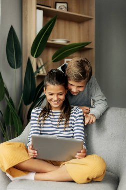 Ablam ve abim evde bir sandalyede oturup tablet üzerinde oynuyorlar. Modern teknoloji ve evde zaman geçirme