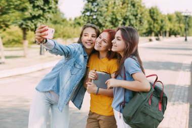 Üç sevimli arkadaş okula giderken telefonlarıyla selfie çekiyorlar. Arkadaşlık kavramı. Eğitim, eğitim, okula dönüş.