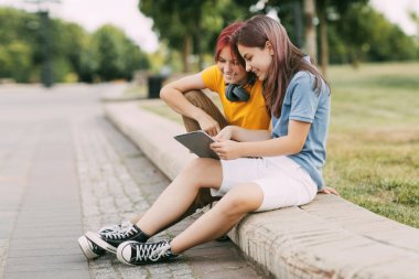 İki çekici kız öğrenci okuldan sonra parkta oturup tablette video izliyorlar ya da ortak bir proje hazırlıyorlar..