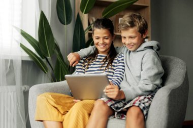 Ablam ve abim evde bir sandalyede oturup tablet üzerinde oynuyorlar. Modern teknoloji ve evde zaman geçirme