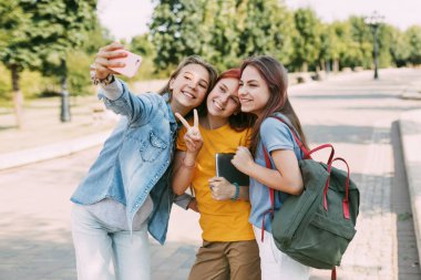 Üç sevimli arkadaş okula giderken telefonlarıyla selfie çekiyorlar. Arkadaşlık kavramı. Eğitim, eğitim, okula dönüş.