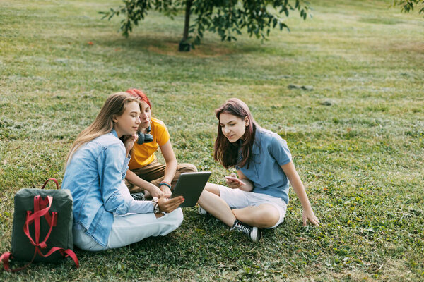 Подростки сидят на зеленой лужайке в парке во время перерыва. Образование и знания, образ жизни подростков