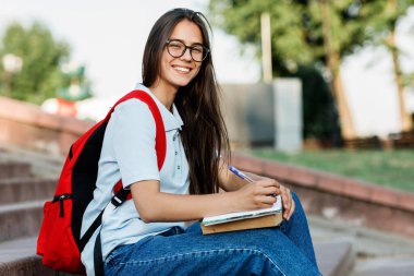 Şehirde merdivenlerde oturan gözlüklü çekici bir kızın portresi.
