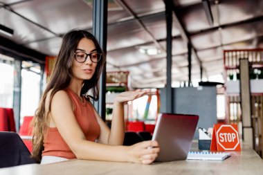 Çekici bir kız bir kafede dijital tablet cihazıyla sohbet ederken arkadaşlarıyla konuşuyor..