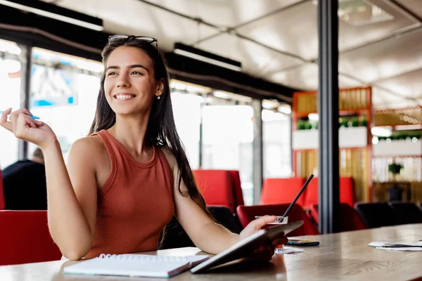 Uma linda garota com um caderno e um tablet está sentada em um café e estudando ou trabalhando — Fotografia de Stock