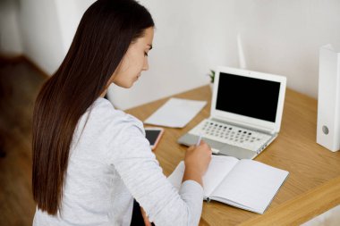 Öğrenci bir kız eğitime hazırlanmak için dizüstü bilgisayar kullanıyor. Not defterine not alıyor. Modern teknolojiler, çevrimiçi eğitim, eğitim