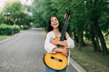 Çekici bir gitarist, yaz parkında yürürken en sevdiği enstrümana sarılıyor. Yaz zamanı, müzik, müzisyen