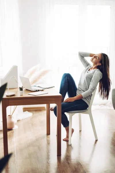 Uma linda garota está sentada inclinada para trás em uma cadeira e se alongando depois do trabalho em um laptop — Fotografia de Stock