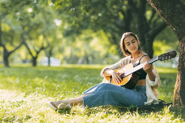 Dívka v harmonii sama se sebou hraje na kytaru v parku. Koníčky, hudba, hudebník — Stock fotografie