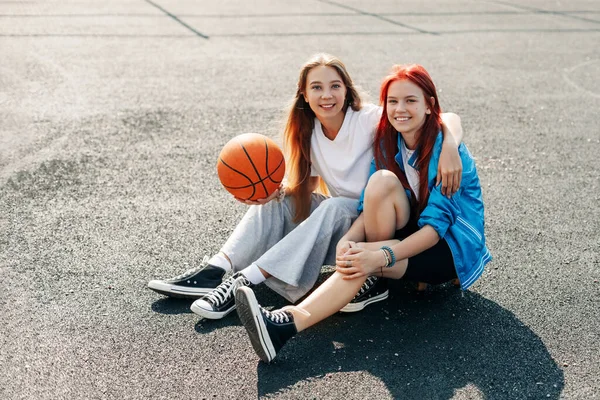 Un par de chicas adolescentes en una cancha deportiva callejera con un estilo de vida de baloncesto relajarse después de un juego y hablar. El concepto de deporte y un estilo de vida saludable — Foto de Stock