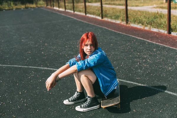 Nettes Teenager-Mädchen sitzt nachmittags auf einem Skateboard im Freien — Stockfoto