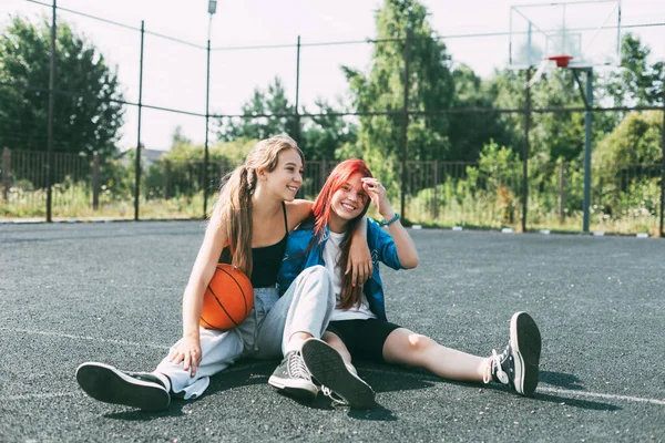 Dvě dívky ve sportovním oblečení a s basketbalem si povídají, sedí na hřišti. Sport, soutěž, přátelství — Stock fotografie