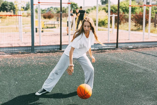 เด็กสาววัยรุ่นนําบาสเกตบอลในสนามกีฬา เด็กผู้หญิงปกป้องลูกบอลระหว่างเกม — ภาพถ่ายสต็อก