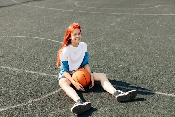 En sjarmerende tenåringsjente med basketball hviler etter trening. Ei jente på idrettsbanen. Sport, trening, sunn livsstil – stockfoto