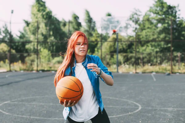 Un jeune joueur de basket-ball s'entraîne sur un terrain de basket-ball extérieur, une adolescente joue au basket-ball. Basket-ball, sport — Photo