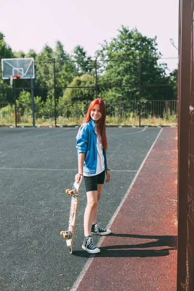 Portrait d'une charmante fille avec une planche à roulettes à la main sur un terrain de sport — Photo