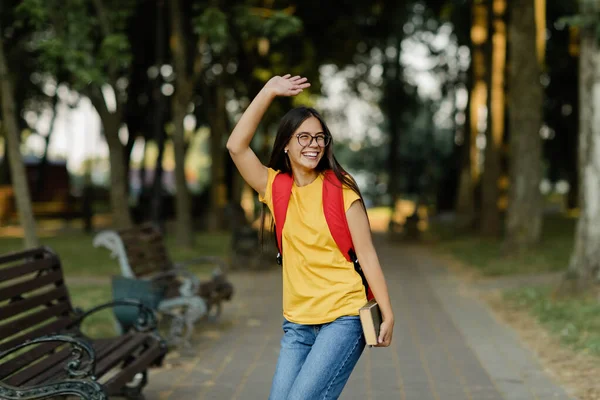 Uma jovem feliz com um livro em suas mãos caminha pelo parque após palestras na universidade — Fotografia de Stock