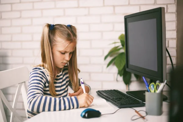 La colegiala se sienta en la computadora y hace su tarea. El niño aprende de casa. Aprendizaje a distancia online. —  Fotos de Stock