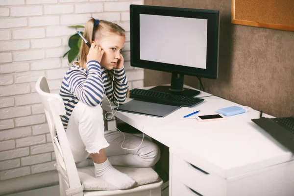 Una chica en auriculares se sienta en una mesa en el ordenador en casa y hace su tarea Educación en línea. El niño aprende de casa. Aprendizaje a distancia online. —  Fotos de Stock