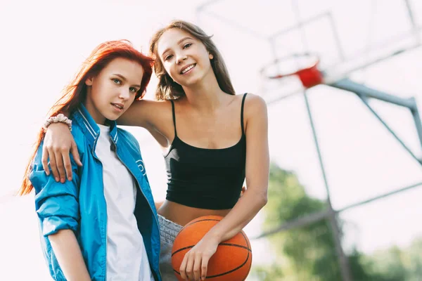 Duas garotas sorridentes estão de pé no campo de basquete — Fotografia de Stock