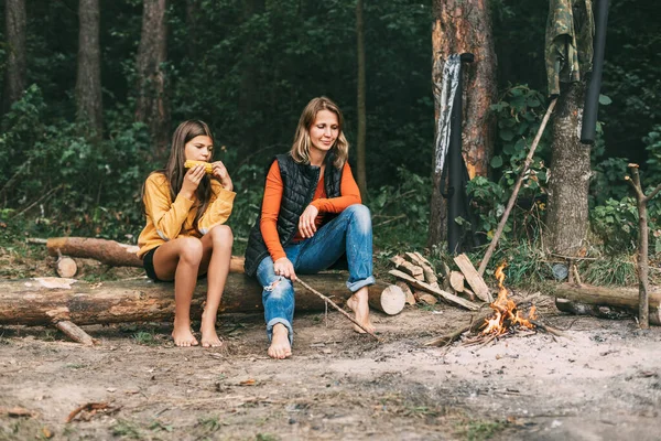 한 어머니가 십 대 딸 과 함께 숲 속이나 공원의 모닥불 근처 의나무에 앉아 있다. 주말, 휴가, 함께 보내는 시간 — 스톡 사진