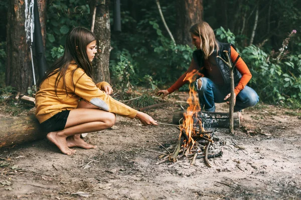 Eine Mutter sitzt mit ihrer halbwüchsigen Tochter auf einem Baum in der Nähe eines Lagerfeuers im Wald oder Park bei einem Picknick. Wochenenden, Urlaub, gemeinsame Zeit — Stockfoto
