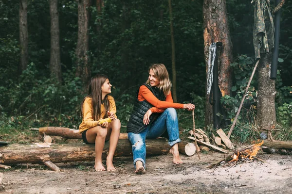 Μια μητέρα με την έφηβη κόρη της κάθεται σε ένα δέντρο κοντά σε μια φωτιά στο δάσος ή πάρκο κατά τη διάρκεια ενός πικ-νικ. Σαββατοκύριακα, διακοπές, χρόνο μαζί — Φωτογραφία Αρχείου