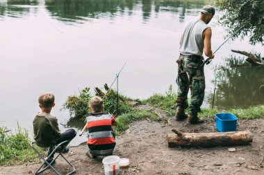 Genç bir adam çocuklarına kamp alanında aile tatili sırasında balık tutmayı öğretiyor. Hobiler, tatiller, hafta sonları, balıkçılık