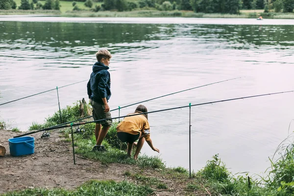 Ένας αδερφός και μια αδελφή στέκονται στην όχθη του ποταμού και ψαρεύουν κατά τη διάρκεια οικογενειακών διακοπών σε κάμπινγκ. Χρόνος μαζί, οικογενειακές διακοπές — Φωτογραφία Αρχείου