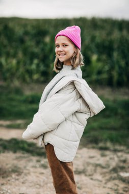 Pembe şapkalı şık görünümlü genç bir kız mısır tarlasının arka planında duruyor.