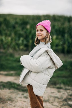 Pembe şapkalı şık görünümlü genç bir kız mısır tarlasının arka planında duruyor.