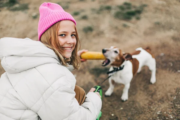 Happy teenage girl hugging and feeding her dog Jack Russell Terrier in a field against the backdrop of a cornfield in autumn — Stock Photo, Image
