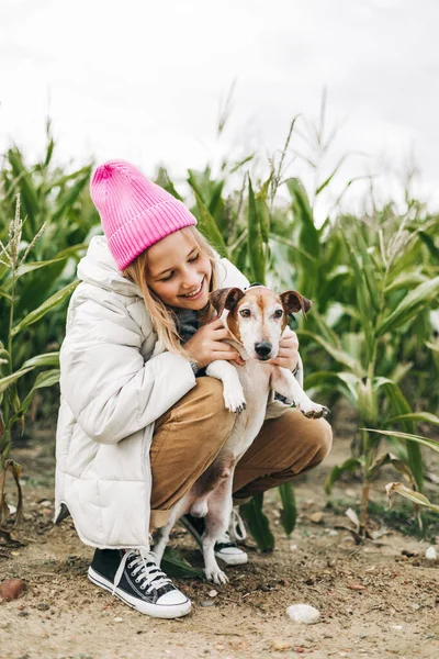 가을에 옥수수밭을 배경으로 들판에서 강아지 잭 러셀 테리어를 껴안고 있는 행복 한 십 대 소녀 — 스톡 사진