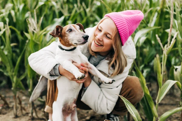 Happy teenage girl hugging her dog Jack Russell terrier in a field against a background of a cornfield in autumn — Stock Photo, Image