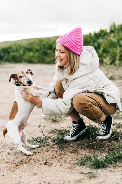 陽気な十代の少女は彼女の犬と一緒にフィールドで遊んでいますジャック・ラッセル・テリア秋のトウモロコシ畑の背景に — ストック写真