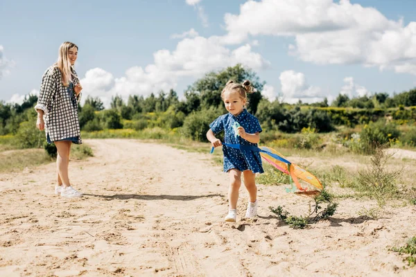 Een klein meisje vliegt een vlieger met haar oudere zus en loopt weg van haar — Stockfoto