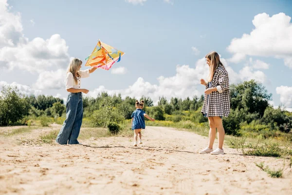 Una madre vola un aquilone con le sue figlie durante una vacanza in famiglia in campagna — Foto Stock