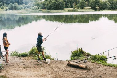 Bir erkek ve kız kardeş bir kamp alanında aile tatili sırasında nehir kıyısında balık tutuyorlar. Birlikte zaman geçirmek, aile tatili.