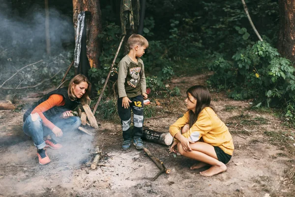 Uma família feliz faz um incêndio durante uma viagem na floresta. Passar tempo juntos, tempo em família — Fotografia de Stock