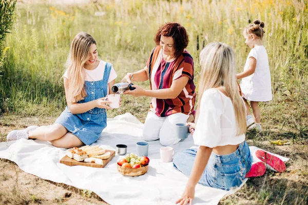 Drie generaties vrouwen van dezelfde familie op een picknick, een grootmoeder schenkt thee uit een thermoskan aan haar dochters en kleindochter — Stockfoto