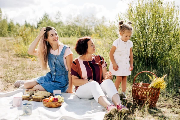 Een grootmoeder en haar twee kleindochters picknicken in de natuur, brengen samen tijd door in het weekend. — Stockfoto